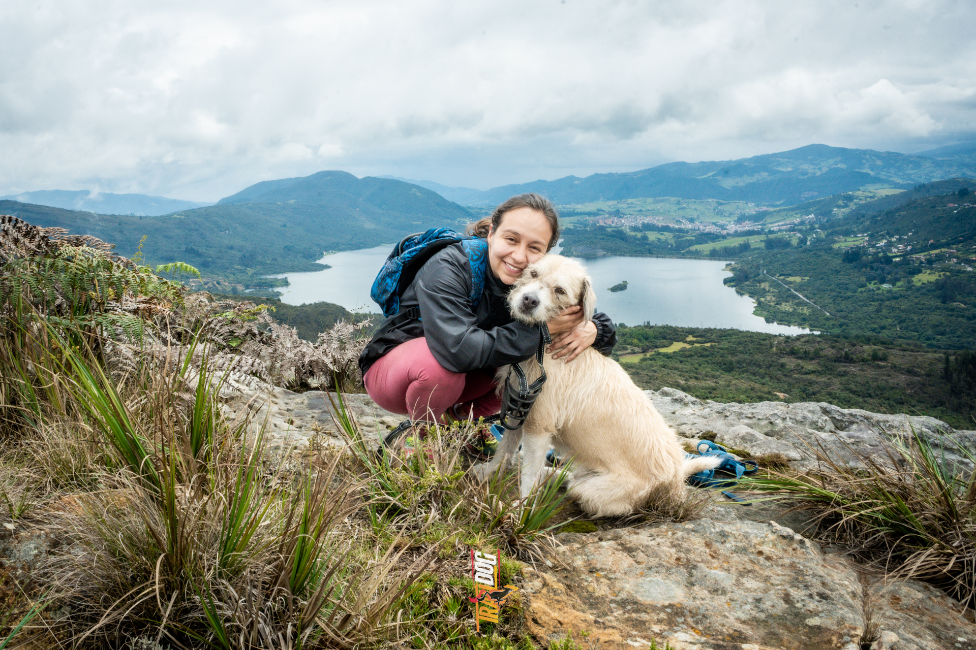 Mujer abrazando a su perro con una laguna de fondo